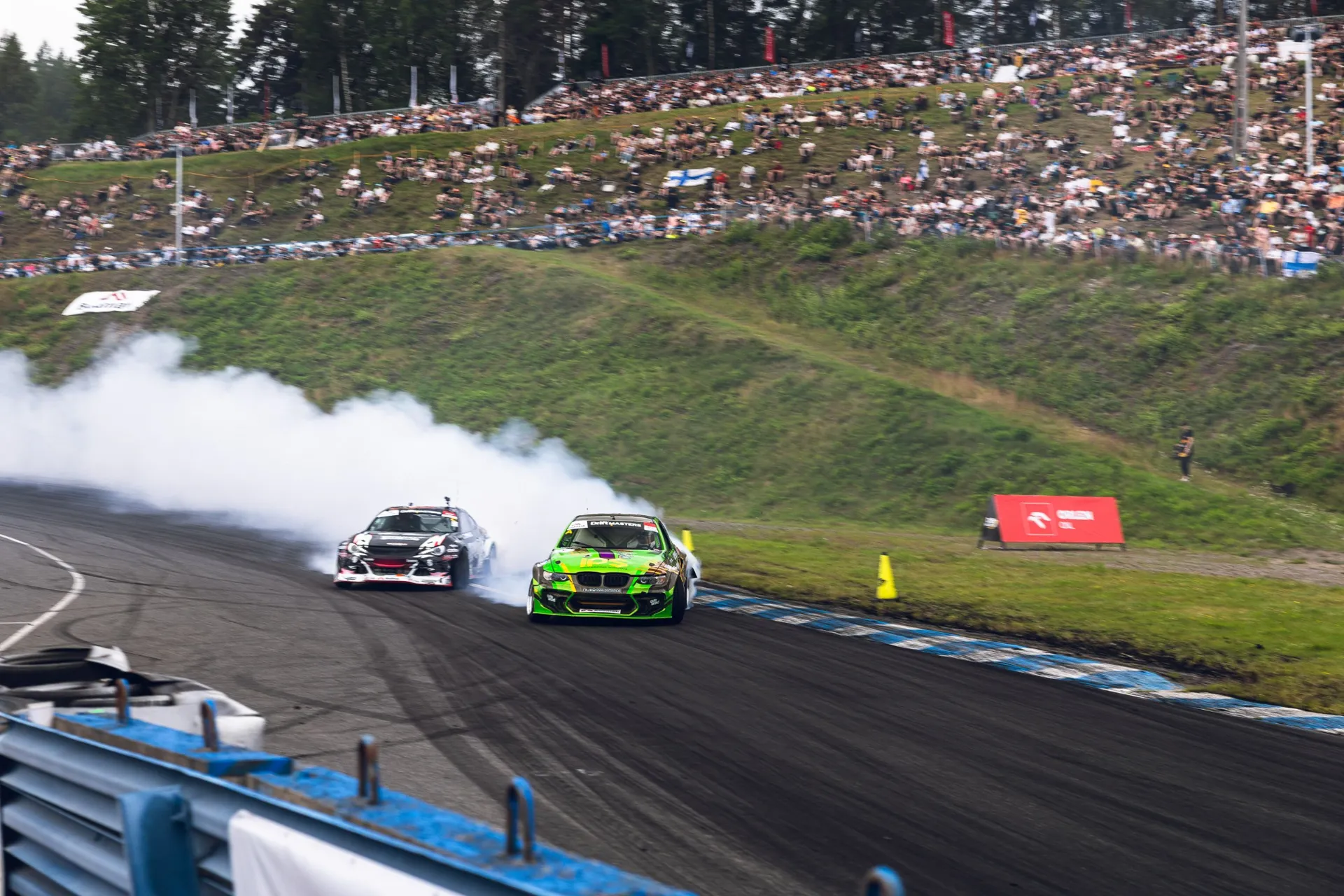 Two drift cars in a tandem battle in front of a packed hillside crowd